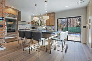 Kitchen featuring wall chimney range hood, high end refrigerator, hanging light fixtures, and backsplash