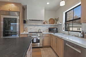 Kitchen with decorative backsplash, high quality appliances, light stone counters, and sink