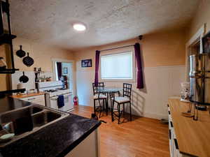 Kitchen with butcher block counters, a textured ceiling, white range with gas cooktop, white cabinets, and light hardwood / wood-style flooring