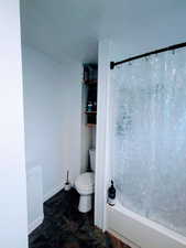 Bathroom featuring a textured ceiling, shower / bath combo with shower curtain, and toilet