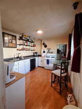 Kitchen with white gas stove, black dishwasher, white cabinetry, light wood-type flooring, and sink