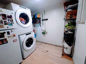 Clothes washing area featuring light wood-type flooring and stacked washer and clothes dryer