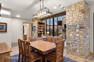 Dining space featuring light wood-type flooring, a wall unit AC, and a notable chandelier