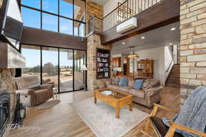 Living room featuring a high ceiling, an AC wall unit, wood-type flooring, and a stone fireplace