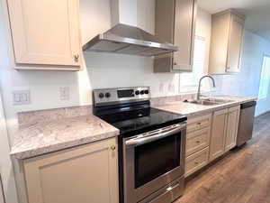 Kitchen with light stone counters, hardwood / wood-style flooring, wall chimney exhaust hood, stainless steel appliances, and sink