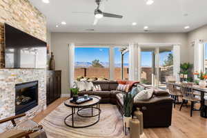 Living room featuring ceiling fan, a stone fireplace, a mountain view, and light wood-type flooring