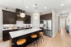 Kitchen with sink, custom exhaust hood, hanging light fixtures, a center island with sink, and appliances with stainless steel finishes