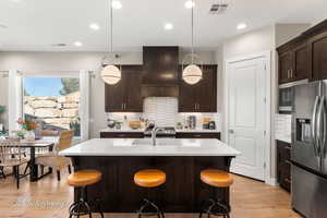 Kitchen featuring custom exhaust hood, hanging light fixtures, a kitchen breakfast bar, and stainless steel fridge with ice dispenser