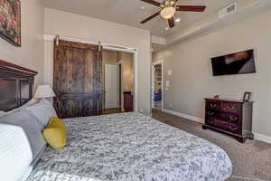 Bedroom with ceiling fan, ensuite bathroom, a barn door, and carpet floors