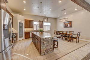 Kitchen featuring a center island, stainless steel appliances, hanging light fixtures, light stone counters, and a breakfast bar