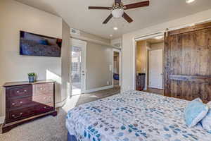 Bedroom with light carpet, connected bathroom, ceiling fan, and a barn door