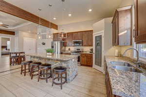 Kitchen featuring appliances with stainless steel finishes, a center island, sink, a breakfast bar, and beam ceiling