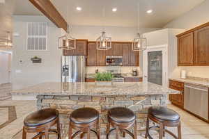 Kitchen with a kitchen island, stainless steel appliances, beamed ceiling, hanging light fixtures, and a breakfast bar area