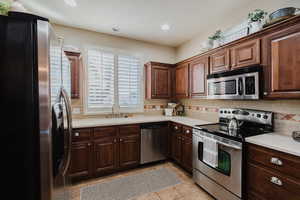 Kitchen featuring tasteful backsplash, sink, dark brown cabinetry, stainless steel appliances, and light tile patterned flooring