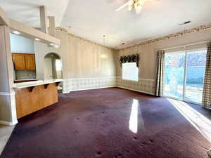 Kitchen with kitchen peninsula, ceiling fan, decorative light fixtures, dark colored carpet, and a kitchen bar