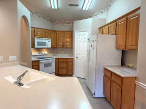 Kitchen featuring white appliances, light tile patterned floors, sink, kitchen peninsula, and lofted ceiling