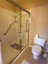 Bathroom with toilet, tile patterned flooring, and a shower with shower door