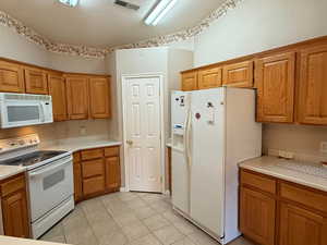 Kitchen with white appliances, a textured ceiling, light tile patterned floors, and lofted ceiling