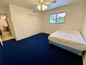 Carpeted bedroom featuring ceiling fan and a closet