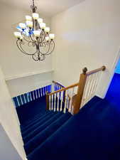 Stairs with a notable chandelier and carpet