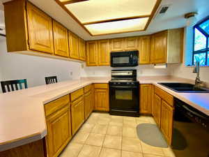 Kitchen with kitchen peninsula, light tile patterned floors, black appliances, and sink