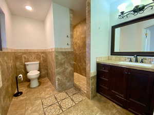 Bathroom featuring toilet, walk in shower, vanity, tile walls, and a notable chandelier