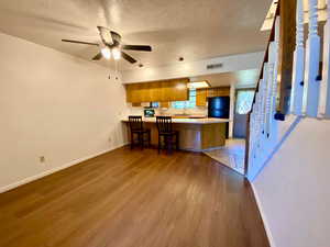 Kitchen featuring kitchen peninsula, a textured ceiling, light hardwood / wood-style flooring, black refrigerator, and a breakfast bar area