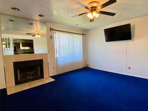 Unfurnished living room featuring carpet floors, a textured ceiling, a tiled fireplace, and ceiling fan