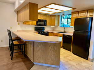 Kitchen featuring sink, light tile patterned floors, kitchen peninsula, black appliances, and a breakfast bar