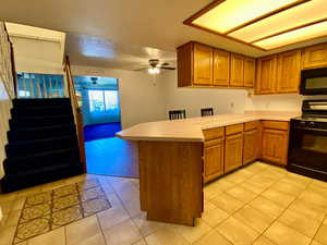 Kitchen with black appliances, ceiling fan, kitchen peninsula, and light tile patterned floors