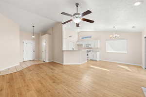 Unfurnished living room featuring a textured ceiling, light hardwood / wood-style flooring, lofted ceiling, and ceiling fan with notable chandelier