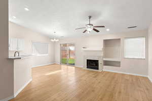 Unfurnished living room with a textured ceiling, vaulted ceiling, a tile fireplace, light hardwood / wood-style floors, and ceiling fan with notable chandelier