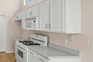 Kitchen with white appliances, light hardwood / wood-style floors, and white cabinets