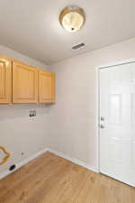 Laundry room featuring a textured ceiling, light wood-type flooring, hookup for a washing machine, and cabinets