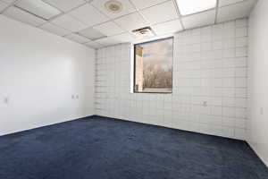 Unfurnished room with dark carpet and a drop ceiling