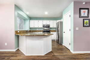 Kitchen featuring kitchen peninsula, white cabinetry, stainless steel appliances, and dark stone counters