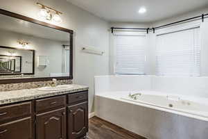 Bathroom featuring tiled bath, wood-type flooring, and vanity