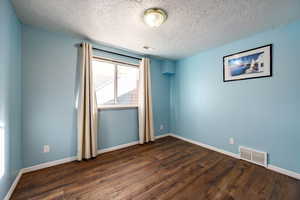 Empty room with a textured ceiling and dark hardwood / wood-style floors