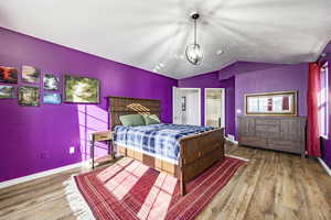 Bedroom featuring hardwood / wood-style flooring, connected bathroom, vaulted ceiling, and an inviting chandelier