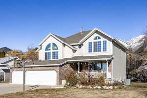 View of front of house with cooling unit, a porch, a garage, a front yard, and a mountain view