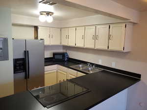 Kitchen featuring black appliances, white cabinets, a textured ceiling, and sink