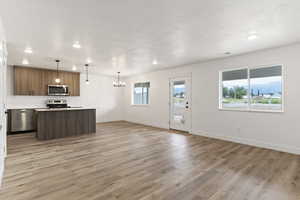 Kitchen with pendant lighting, light wood-type flooring, tasteful backsplash, a textured ceiling, and stainless steel appliances