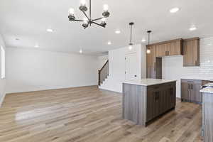 Kitchen with decorative light fixtures, decorative backsplash, a center island, and light hardwood / wood-style flooring