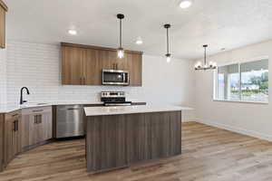 Kitchen with light wood-type flooring, backsplash, hanging light fixtures, and appliances with stainless steel finishes