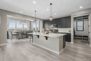 Kitchen with stainless steel appliances, a center island with sink, a breakfast bar area, and decorative light fixtures