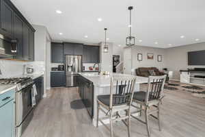 Kitchen with sink, pendant lighting, appliances with stainless steel finishes, and a kitchen island with sink