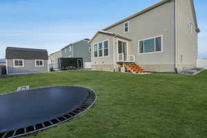 Rear view of property featuring a lawn, an outdoor structure, and a trampoline