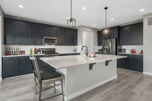 Kitchen featuring a kitchen breakfast bar, hanging light fixtures, sink, an island with sink, and stainless steel appliances