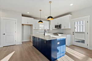 Kitchen with white cabinetry, hanging light fixtures, a kitchen island with sink, sink, and stainless steel appliances