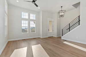 Entryway with ceiling fan with notable chandelier, light hardwood / wood-style flooring, and a high ceiling